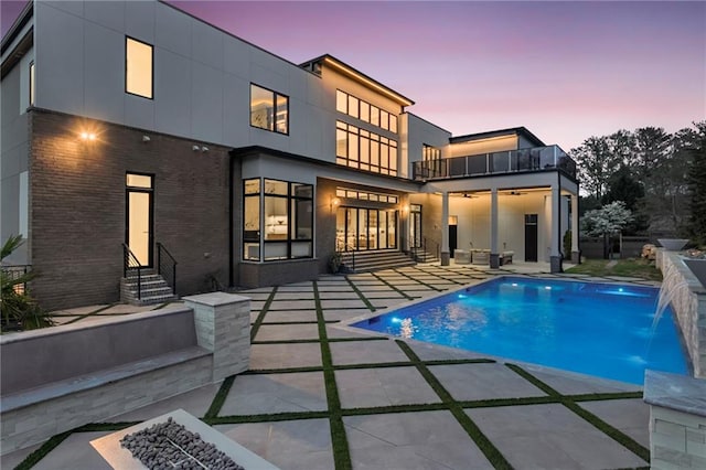 back of property with a balcony, an outdoor pool, a patio area, brick siding, and entry steps
