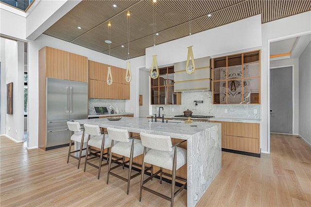 kitchen with a large island with sink, light stone countertops, light wood-type flooring, and stainless steel appliances