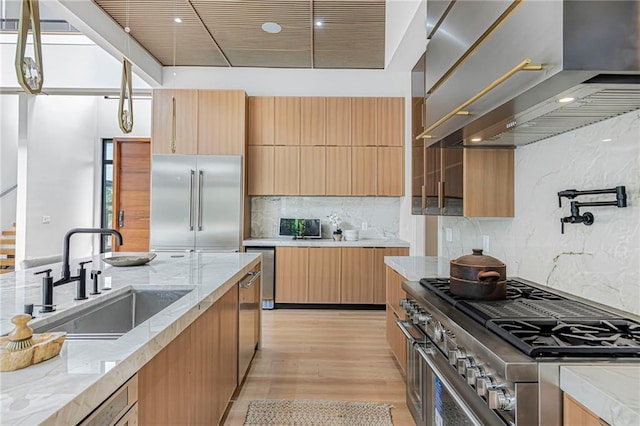 kitchen featuring light stone countertops, modern cabinets, wall chimney exhaust hood, premium appliances, and a sink