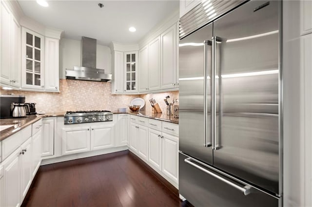 kitchen with stainless steel appliances, decorative backsplash, dark wood-style flooring, and wall chimney range hood