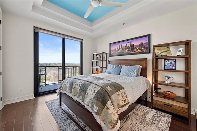 bedroom with access to exterior, ceiling fan, baseboards, a tray ceiling, and hardwood / wood-style floors