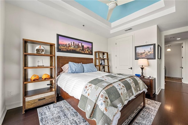 bedroom featuring dark wood finished floors, a tray ceiling, visible vents, and baseboards