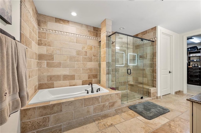 bathroom featuring a bath, a stall shower, a spacious closet, and stone tile flooring