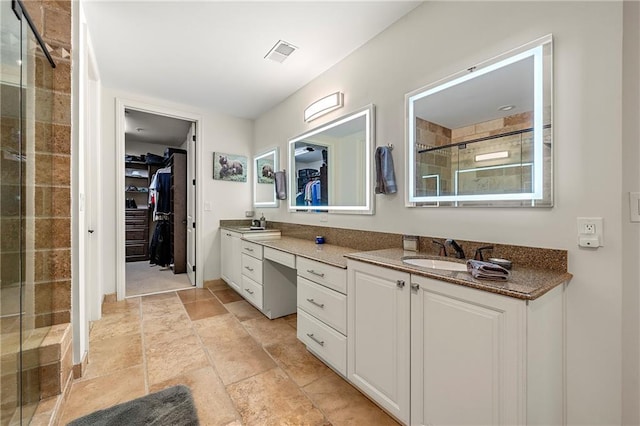 full bath with visible vents, a walk in closet, a sink, a shower stall, and double vanity