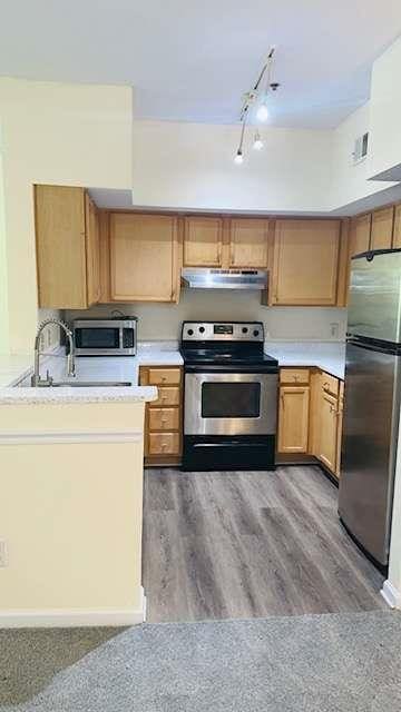 kitchen with appliances with stainless steel finishes, sink, track lighting, and light hardwood / wood-style floors