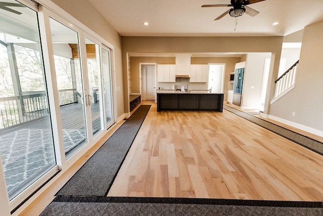 kitchen featuring an island with sink, a ceiling fan, white cabinets, light wood finished floors, and light countertops