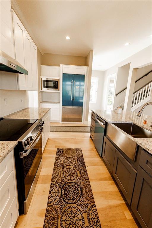 kitchen featuring light stone counters, a sink, white cabinets, built in appliances, and light wood-type flooring