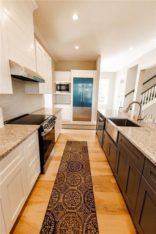 kitchen with under cabinet range hood, stainless steel appliances, light wood-style floors, white cabinetry, and a sink