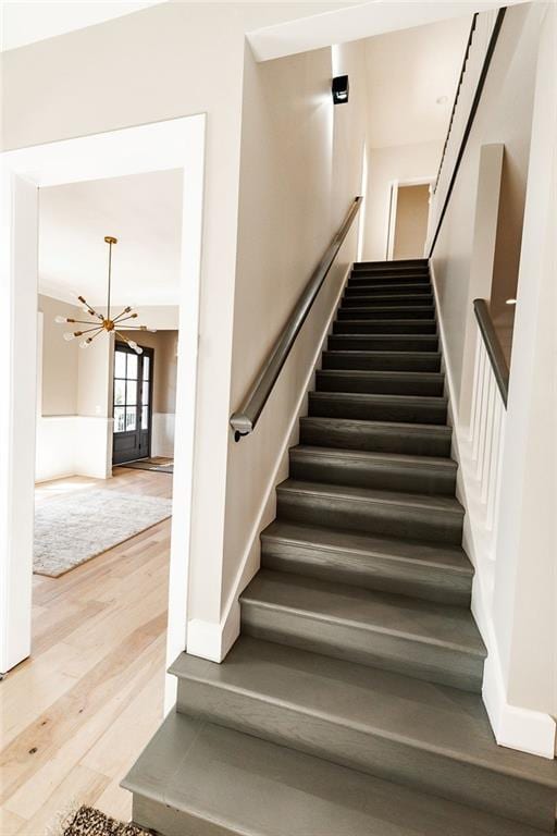 staircase featuring baseboards, a notable chandelier, and wood finished floors