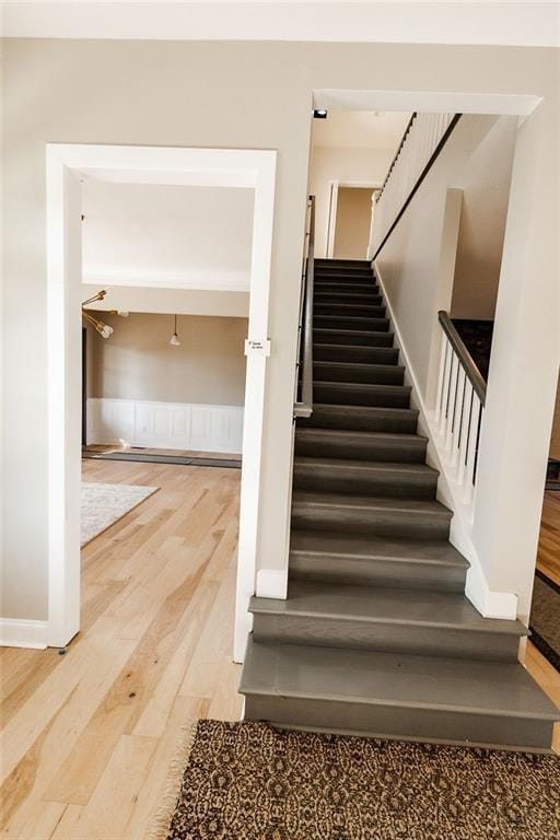 stairs with a wainscoted wall and wood finished floors