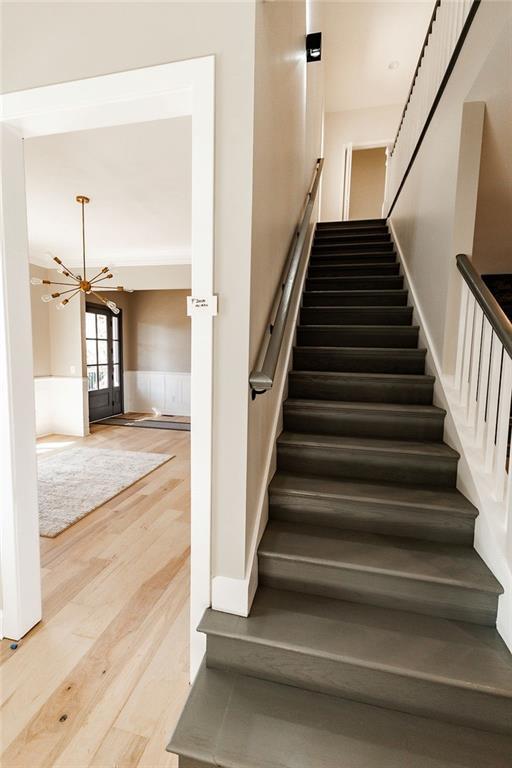 stairs with a notable chandelier, wainscoting, and wood finished floors