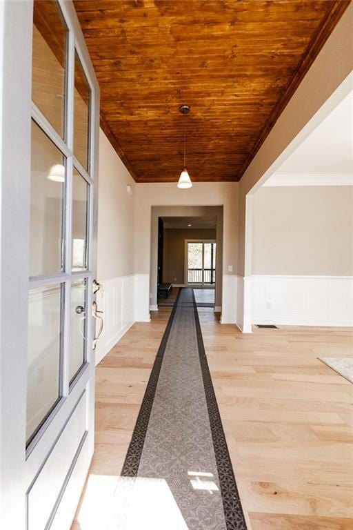 corridor with a wainscoted wall, ornamental molding, a decorative wall, wooden ceiling, and light wood finished floors