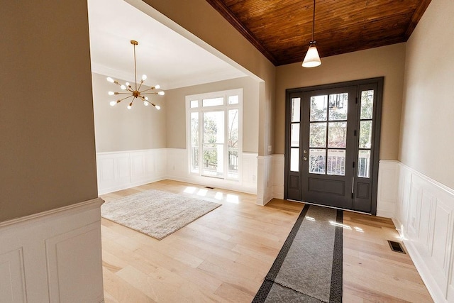 foyer entrance with light wood-type flooring, visible vents, ornamental molding, wooden ceiling, and wainscoting