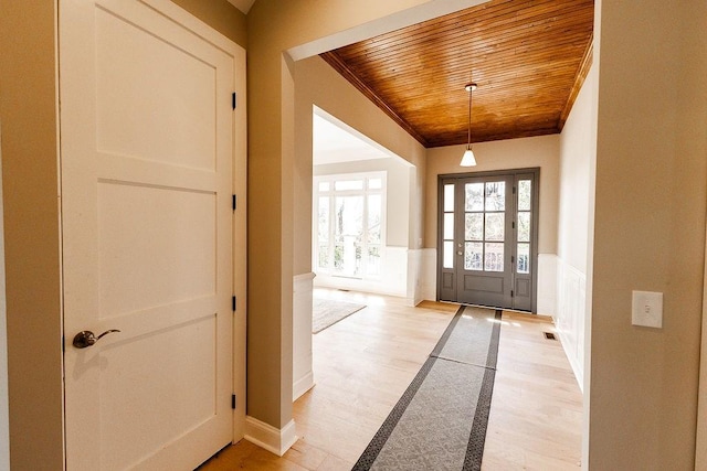 foyer entrance with light wood-style floors, wainscoting, a decorative wall, crown molding, and wood ceiling