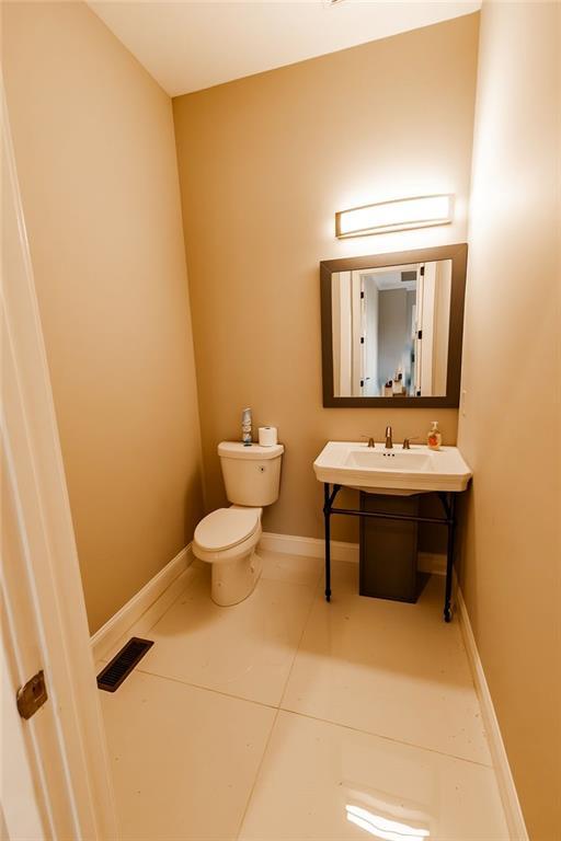 half bath featuring visible vents, baseboards, toilet, tile patterned floors, and a sink