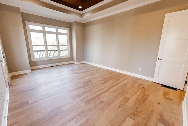 spare room featuring baseboards, a raised ceiling, light wood-style floors, and crown molding