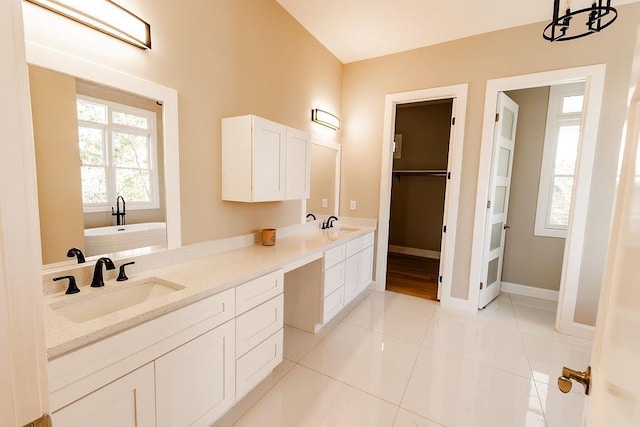 bathroom featuring baseboards, a washtub, double vanity, tile patterned floors, and a sink