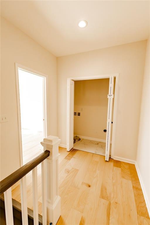 hallway with an upstairs landing, baseboards, and light wood-style flooring