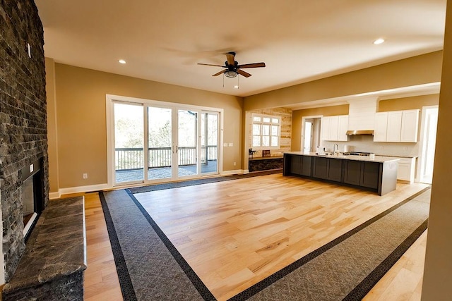 kitchen featuring light wood finished floors, a large fireplace, light countertops, white cabinets, and a ceiling fan