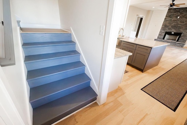 staircase with a large fireplace, ceiling fan, and wood finished floors