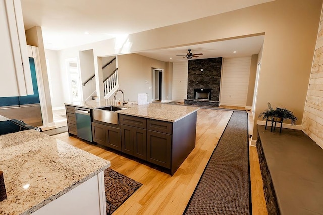 kitchen with light stone counters, ceiling fan, a sink, dishwasher, and light wood-type flooring