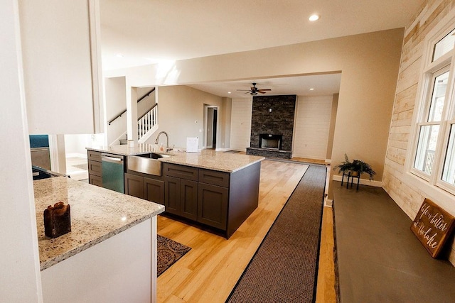 kitchen featuring light wood finished floors, a sink, light stone counters, a fireplace, and stainless steel dishwasher