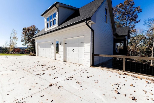 view of property exterior with driveway, fence, a garage, and roof with shingles