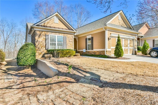 view of front facade with stone siding, a shingled roof, and driveway