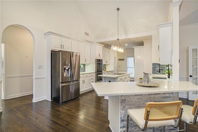 kitchen with dark wood-type flooring, appliances with stainless steel finishes, a center island, white cabinets, and decorative light fixtures