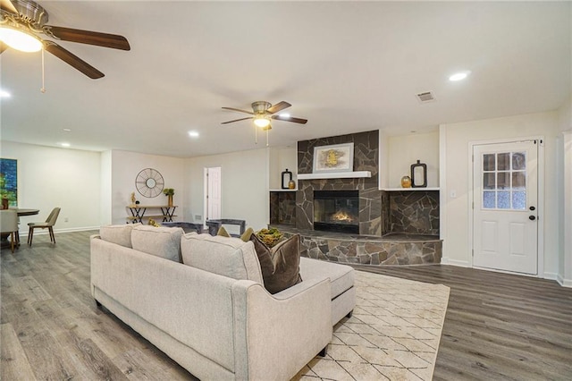 living room with hardwood / wood-style floors, a stone fireplace, and ceiling fan