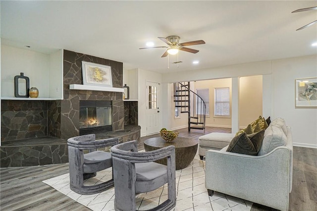 living room with ceiling fan, wood-type flooring, and a stone fireplace