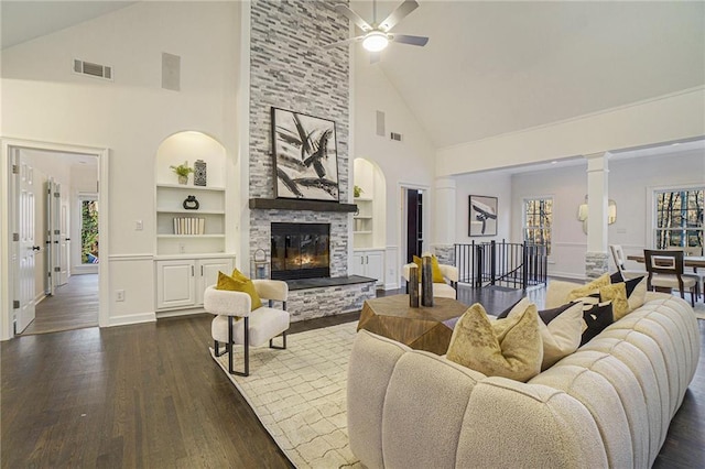 living room with dark hardwood / wood-style flooring, a stone fireplace, built in features, and ornate columns