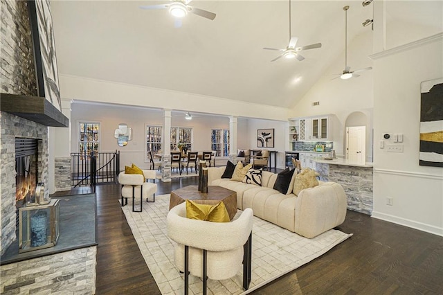 living room featuring dark hardwood / wood-style floors, a fireplace, high vaulted ceiling, and decorative columns