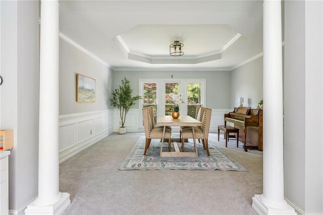 carpeted dining area with a tray ceiling, a wainscoted wall, ornamental molding, and decorative columns