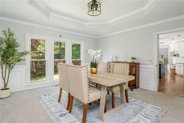 dining space featuring crown molding, a tray ceiling, light colored carpet, and a wainscoted wall