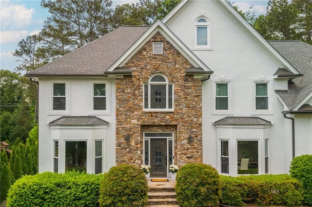 view of front of home featuring roof with shingles, stucco siding, and stone siding
