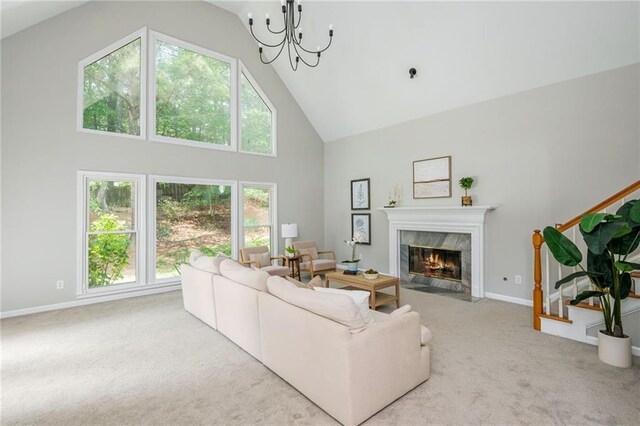 carpeted living area featuring high vaulted ceiling, baseboards, a premium fireplace, and a notable chandelier