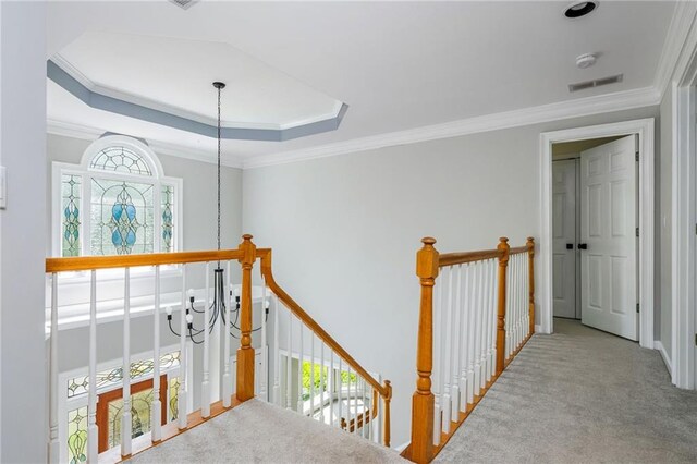 hallway with visible vents, carpet floors, a raised ceiling, an upstairs landing, and ornamental molding