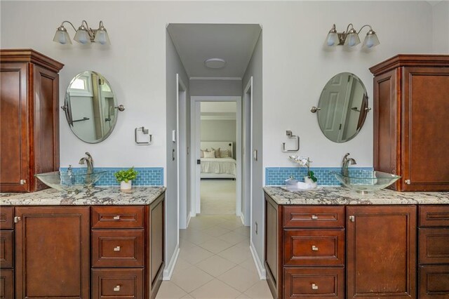 ensuite bathroom with a sink, tile patterned floors, decorative backsplash, and two vanities