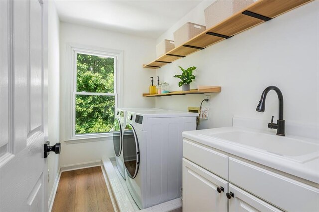 washroom featuring washer and dryer, baseboards, light wood-style flooring, a sink, and cabinet space