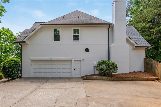 view of home's exterior featuring a shingled roof, an attached garage, stucco siding, a chimney, and concrete driveway
