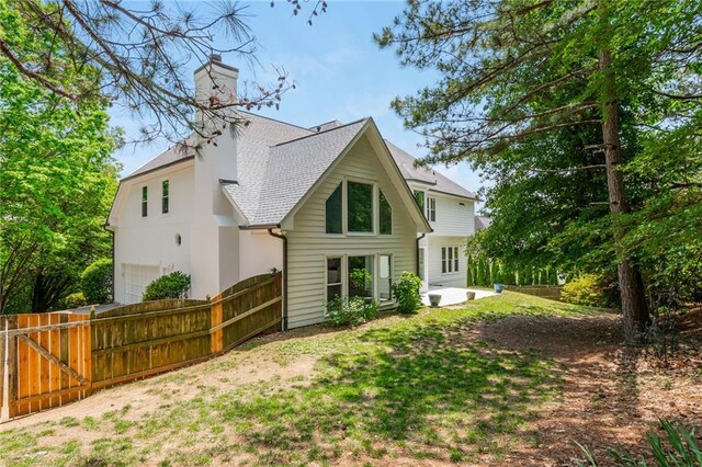 rear view of house featuring fence, a shingled roof, a garage, a chimney, and a patio area