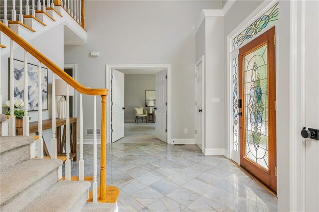 foyer entrance featuring crown molding, marble finish floor, baseboards, visible vents, and stairway