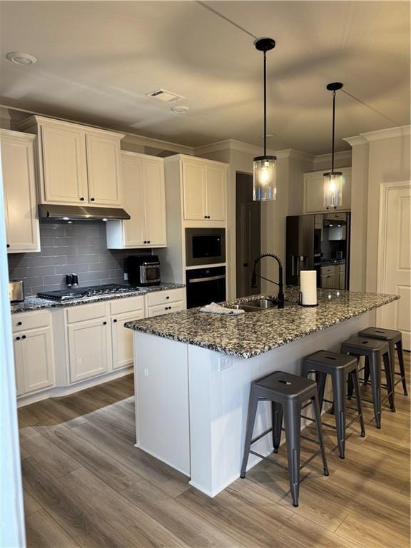 kitchen with wood finished floors, decorative backsplash, oven, and under cabinet range hood