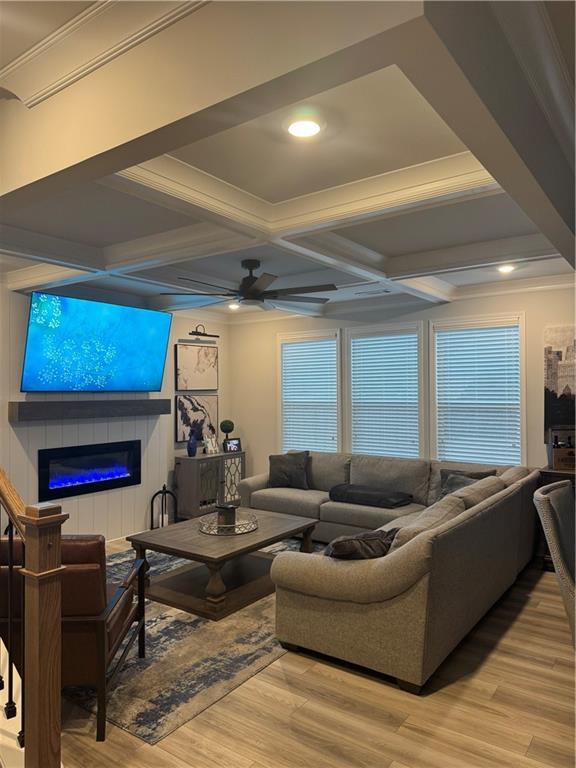 living room featuring a ceiling fan, a glass covered fireplace, coffered ceiling, and wood finished floors