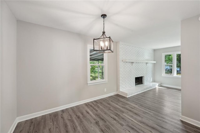 unfurnished living room with wood finished floors, a chandelier, baseboards, and a fireplace