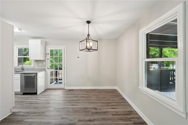 unfurnished dining area with wood finished floors, a sink, a chandelier, and baseboards
