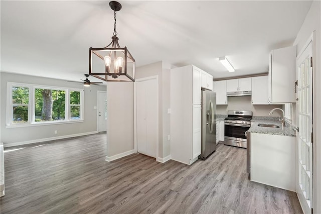kitchen featuring stainless steel appliances, a sink, under cabinet range hood, a chandelier, and light stone counters