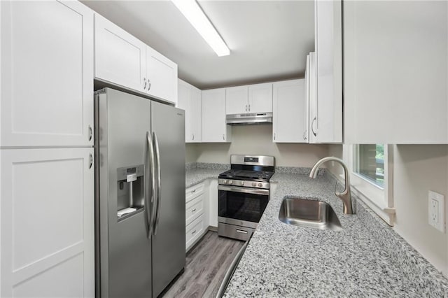 kitchen featuring stainless steel appliances, a sink, under cabinet range hood, white cabinetry, and light stone countertops
