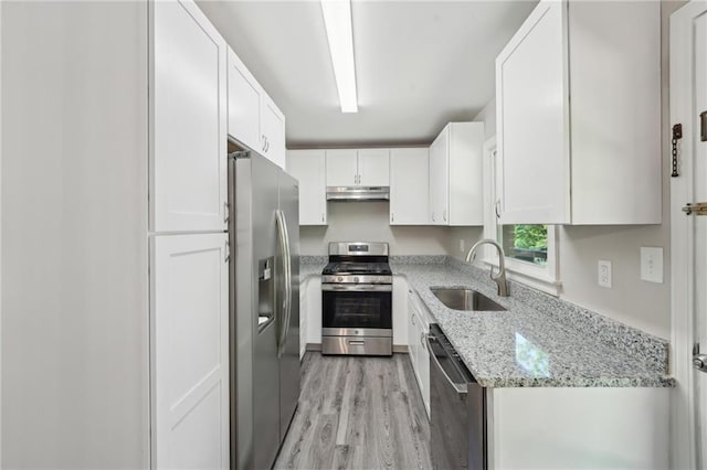 kitchen featuring stainless steel appliances, a sink, under cabinet range hood, light wood finished floors, and white cabinets